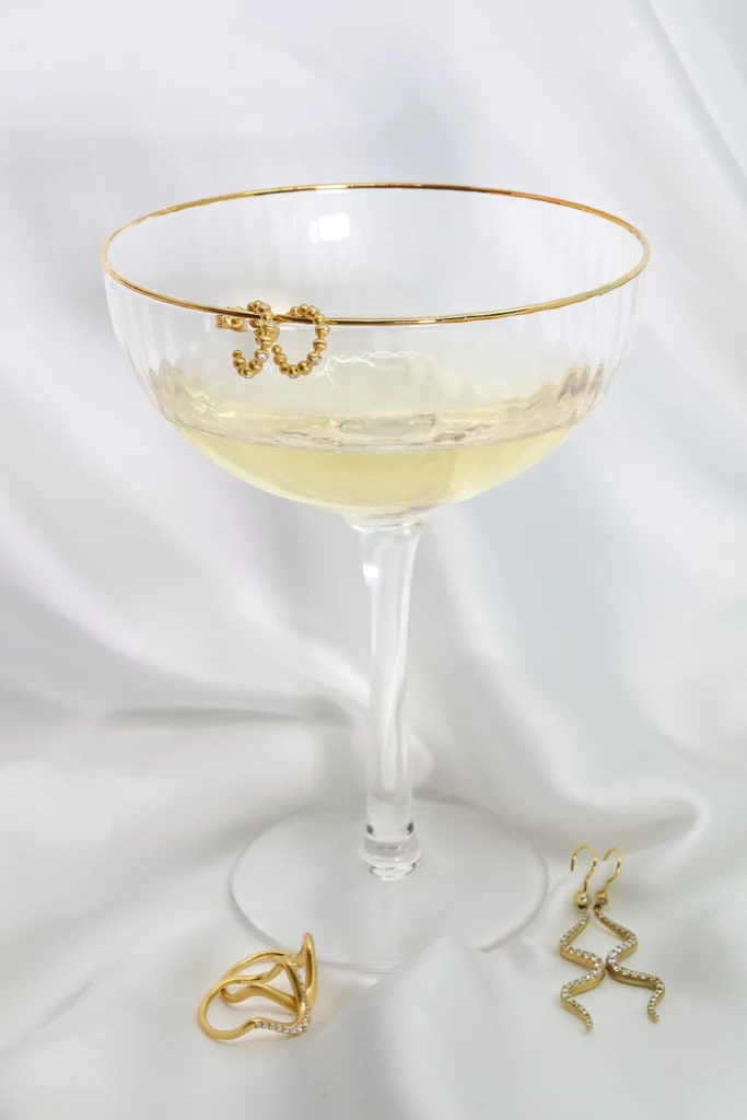 Champagne glass with "Pebbles Small Hoops" on the side and rings and earrings from the "Wave" collection